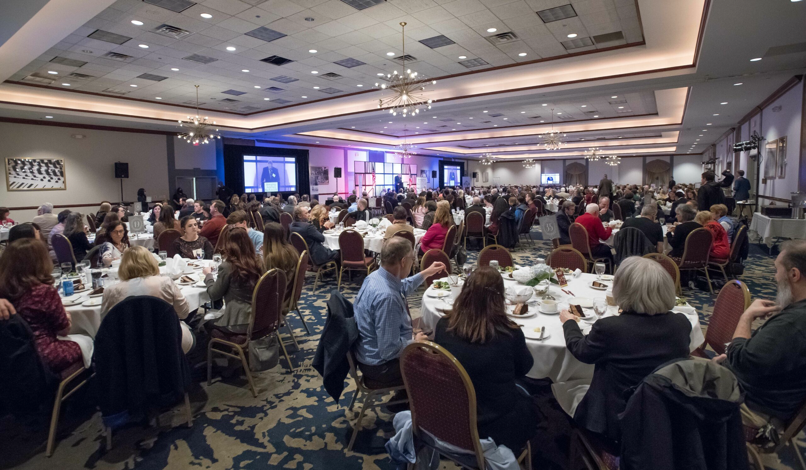 Wide view of an elegant ballroom setup with round tables and sophisticated lighting, representing the professional conference venues that this nonprofit organization manages through their streamlined registration system.